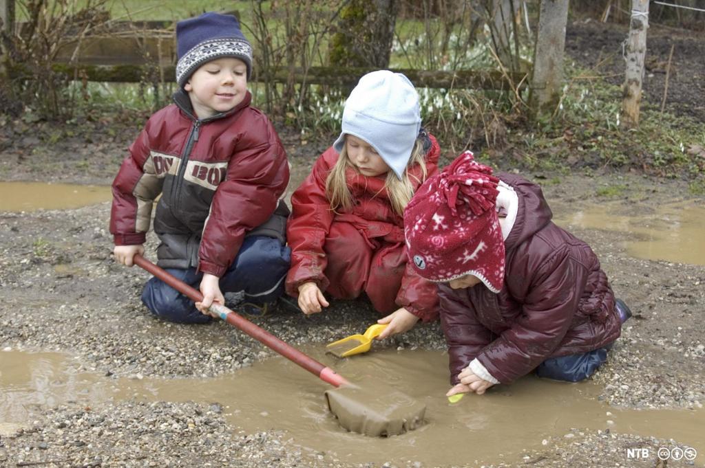 Tre barn leker ute med vann, sand og søle. Foto.