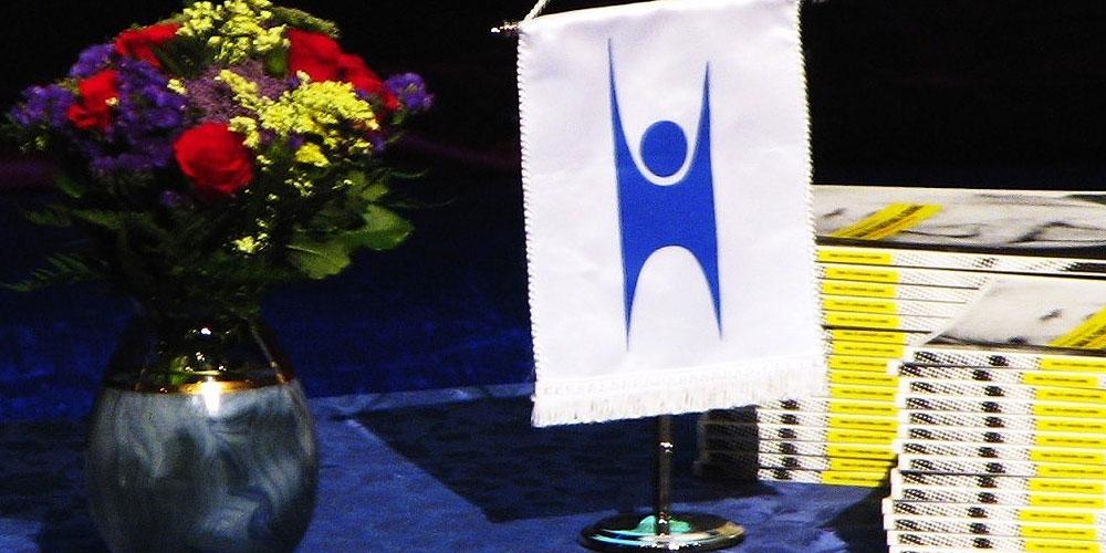 Bord med blå duk, et tent stearinlys og en vimpel med en logo som fremstiller et menneske. Foto.