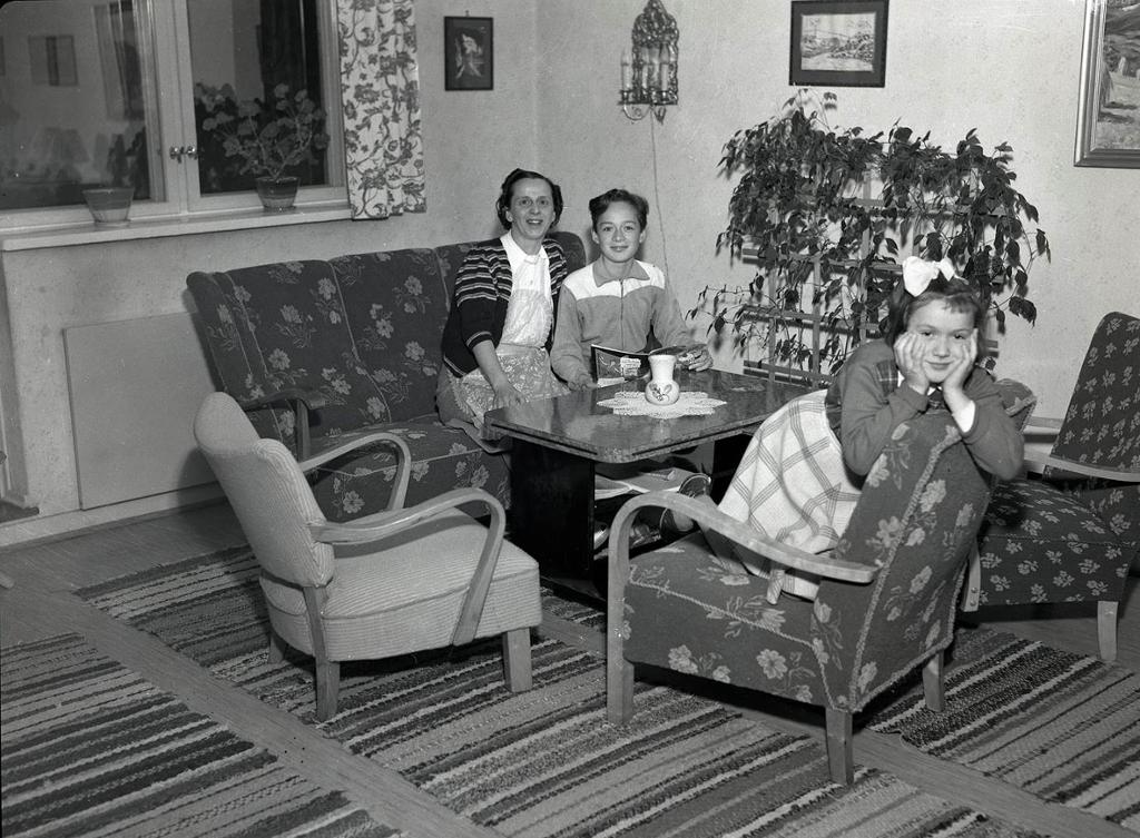 Ei husmor og to barn i ei sittegruppe i ei stue på 1950-tallet. Foto.