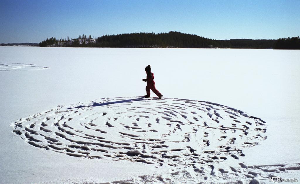 Et barn lager snølabyrint på snødekt is. Foto.