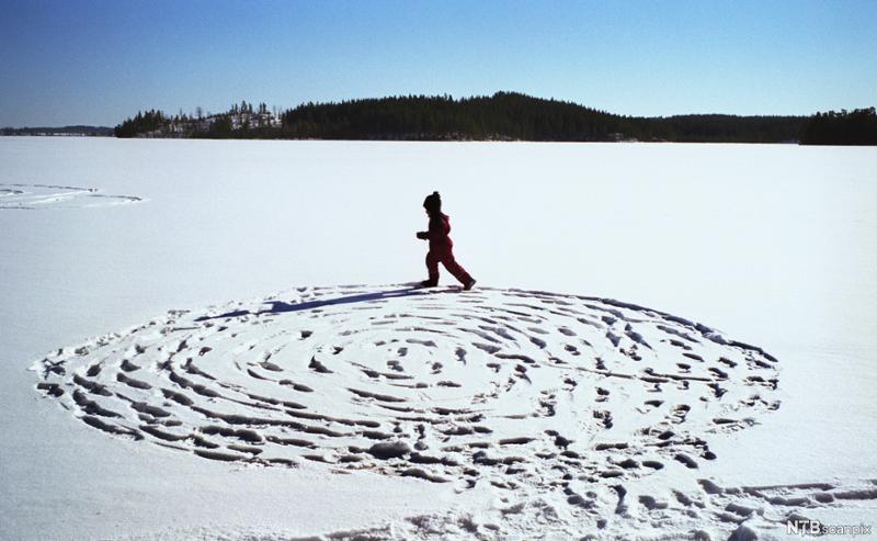 Et barn lager snø-labyrint på snødekt is.