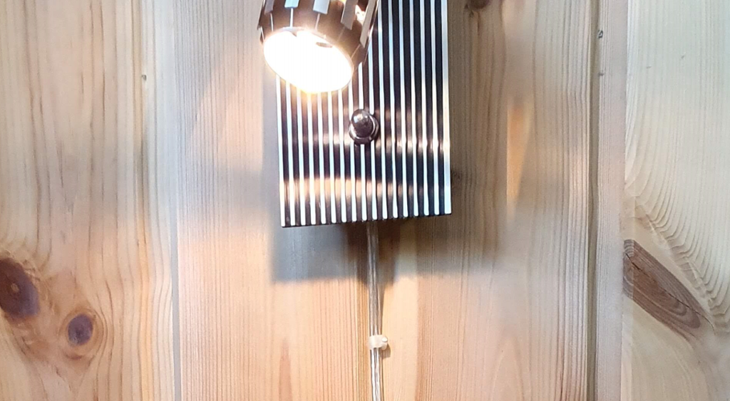 Vegglampe som lyser. Strømledningen til lampen er festet med ledningsklips. Foto.