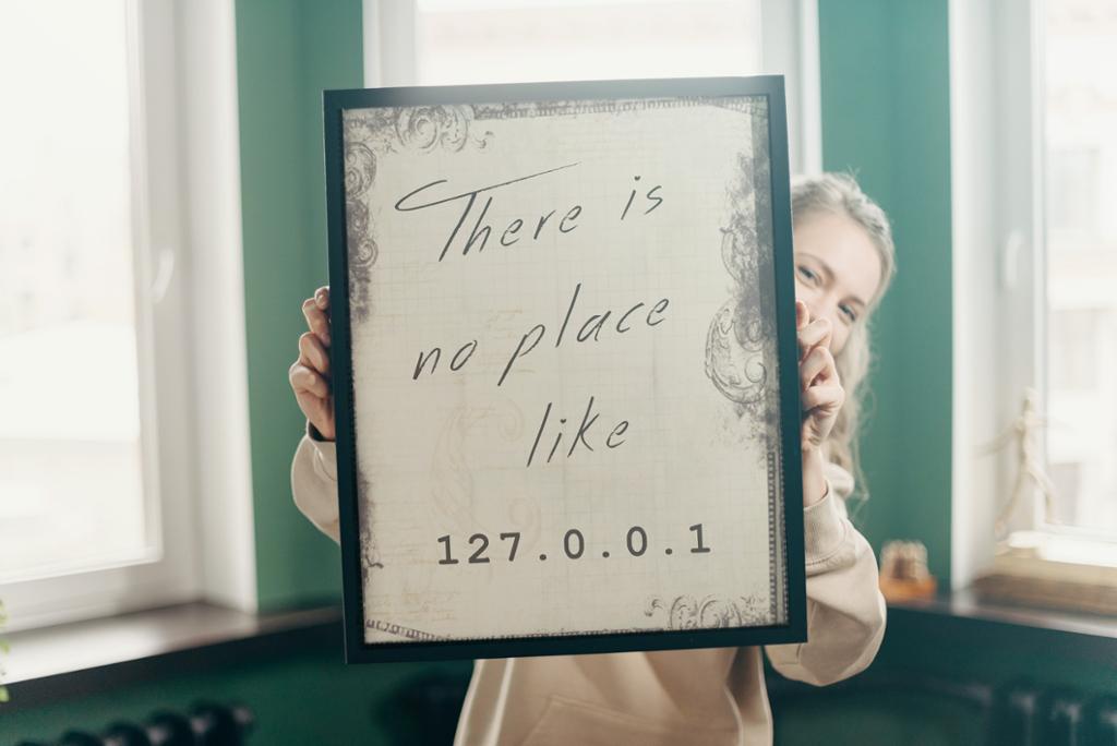 Jente holder opp en innrammet plakat med teksten There is no place like 127.0.0.1. Foto.