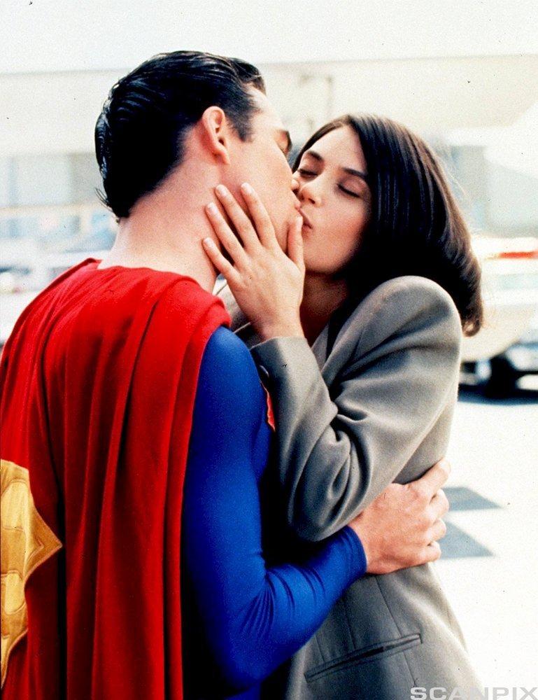 Supermann kyssar Lois Lane. Mann med blå trikot og raud kappe med ein stor, gul S på omfamnar og kyssar ei kvinne med grå blazer. Foto.