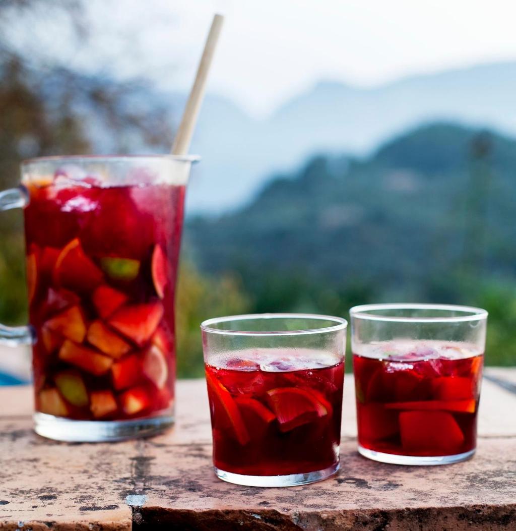 En mugge og to glass med rød drikke med fruktbiter i servert på toppen av en steinmur. Foto.