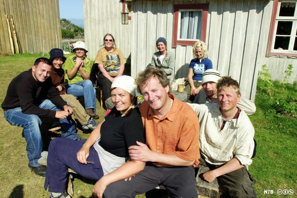 Ei gruppe kvinner og menn i fritidsklær foran et lite gårdsbruk. Foto.