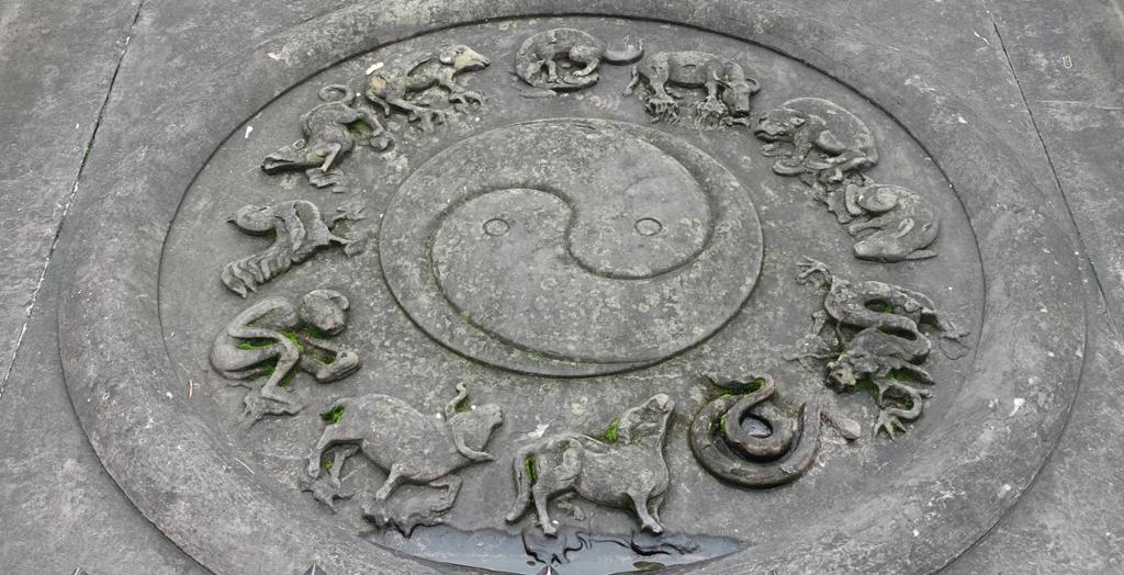 Yin yang-symbol med dyrefigurer rundt støpt i bakken. Foto.