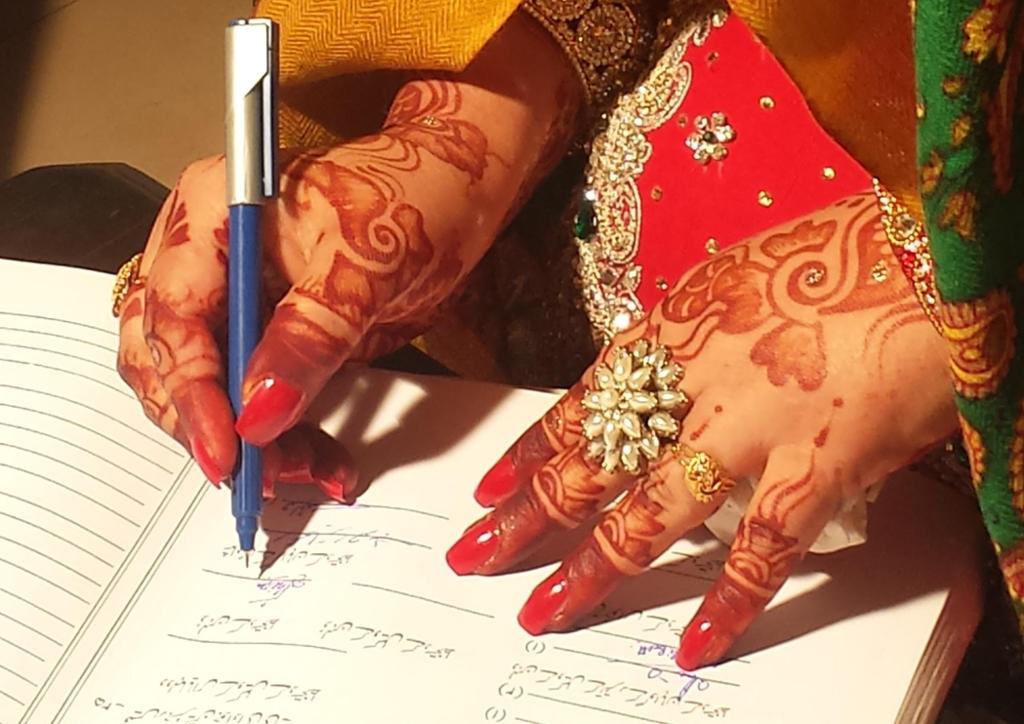 Kvinne med hennamaling på hendene signerer i ei bok. Foto.