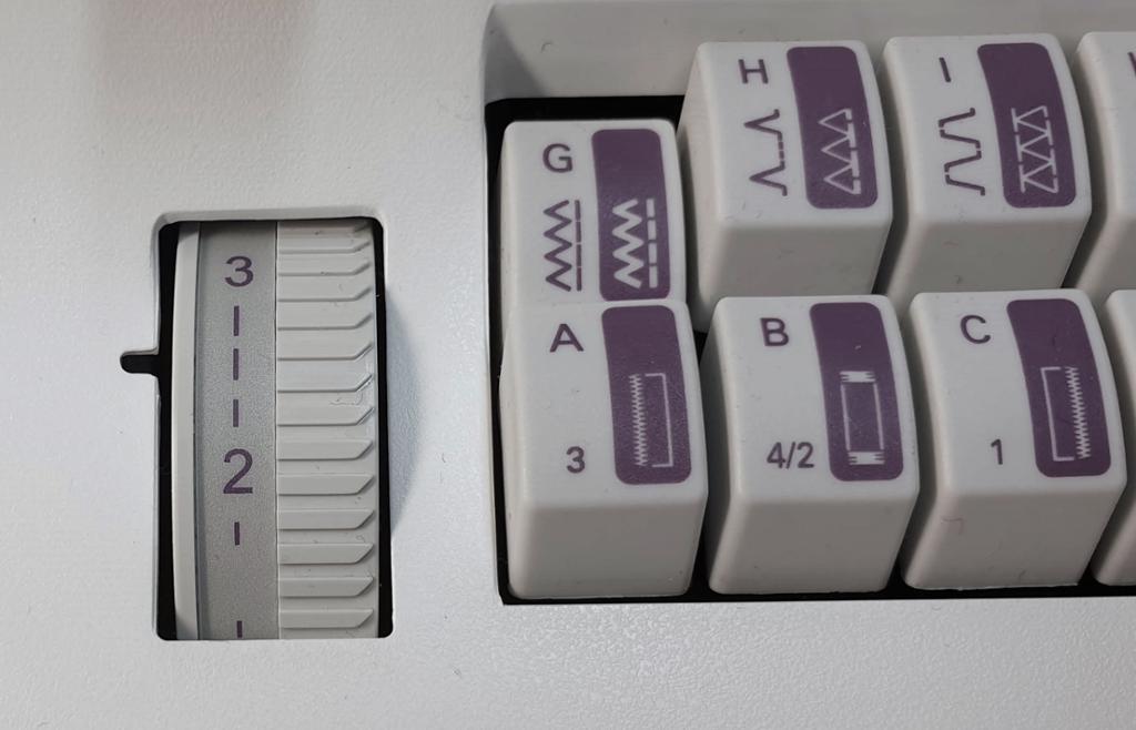 Fotografi av knapper for ulike sømmer på en symaskin og et hjul for stinglengde som er stilt mellom 2 og 3.