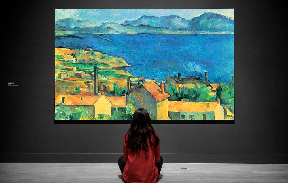 Jente sitter foran et maleri. Foto.
