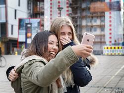 To jenter som ser på en mobil og ler. Foto.