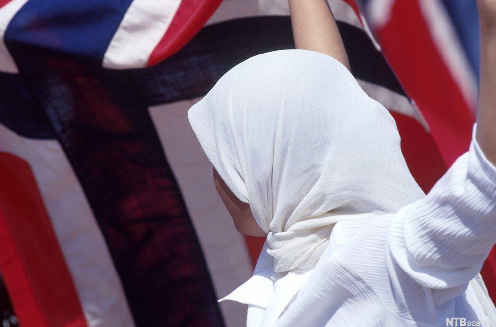 Muslimsk jente med hidjab bærer stort norsk flagg i 17. maitog. Foto.