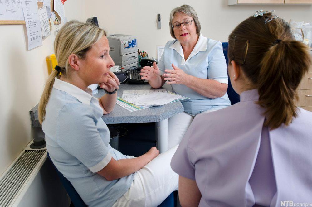 Tre kvinner med sykehusuniformer snakker sammen. Foto. 