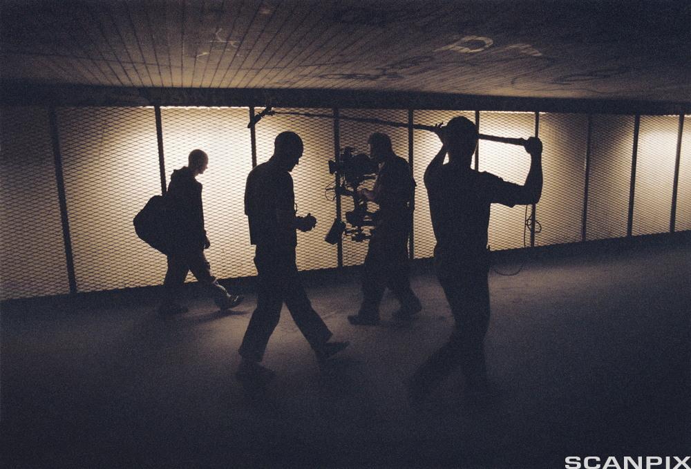 Scene fra en filmproduksjon. Et kamerateam i gang med å filme en mann som går gjennom en mørklagt gang. Foto.