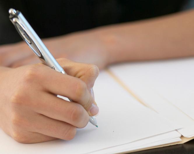 Nærbilde av en hånd som skriver på ark med penn. Foto. 
