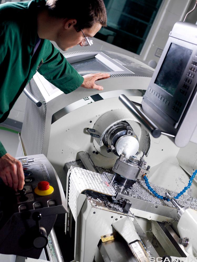 Metallarbeider justerer kontrollene på en CNC dreiebenk. Foto. 