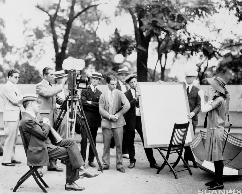 En kvinnelig skuespiller opptrer foran en gruppe menn med filmkamera. Foto.