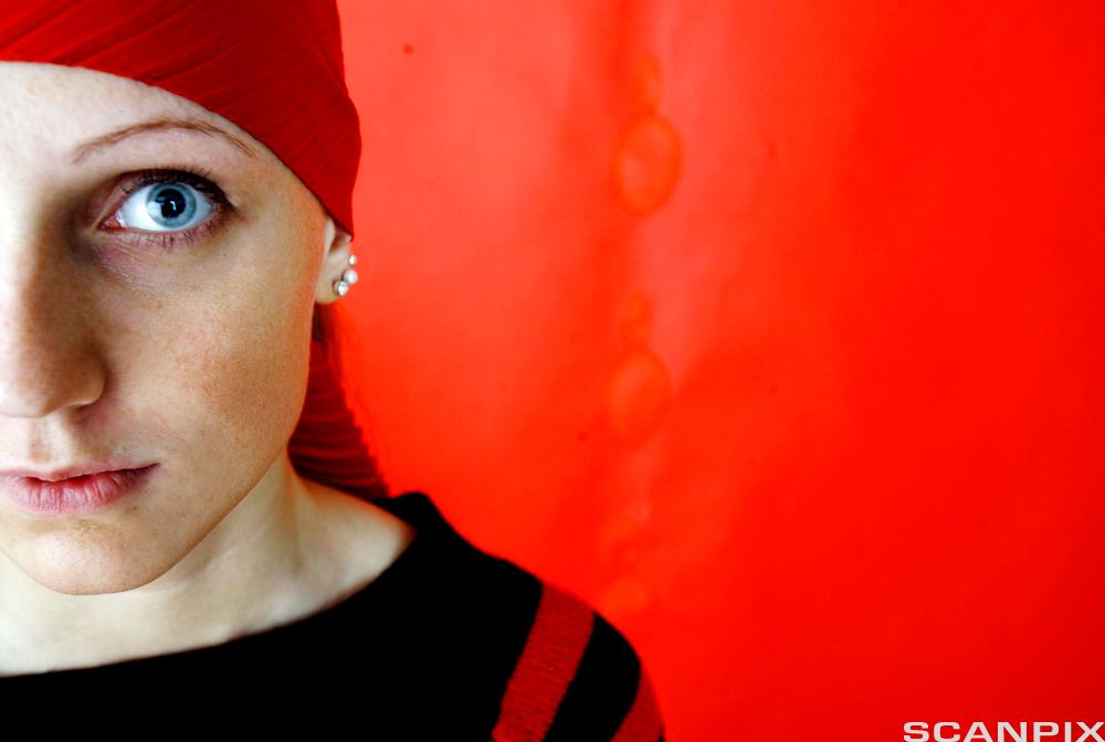 Halvt ansikt av jente mot rød vegg. Foto. 