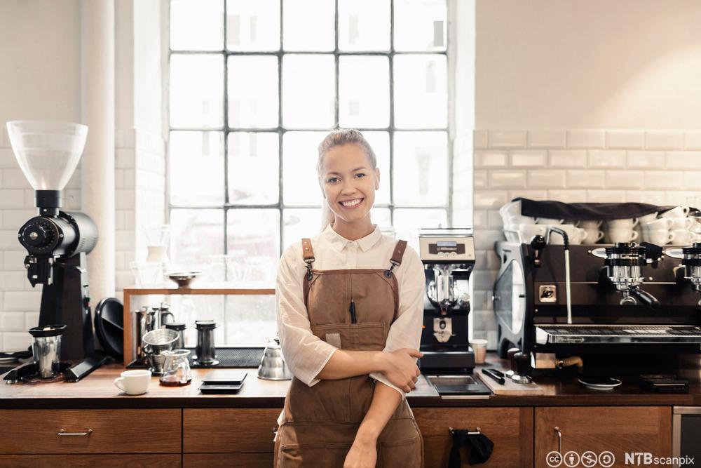 En kvinnelig barista står foran en disk med kaffemaskiner. Foto.