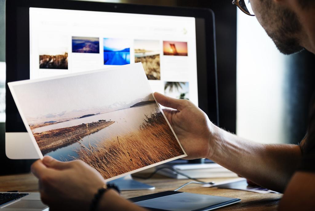 Mann ser på et bilde foran en skjerm med mange ulike bilder. Foto.