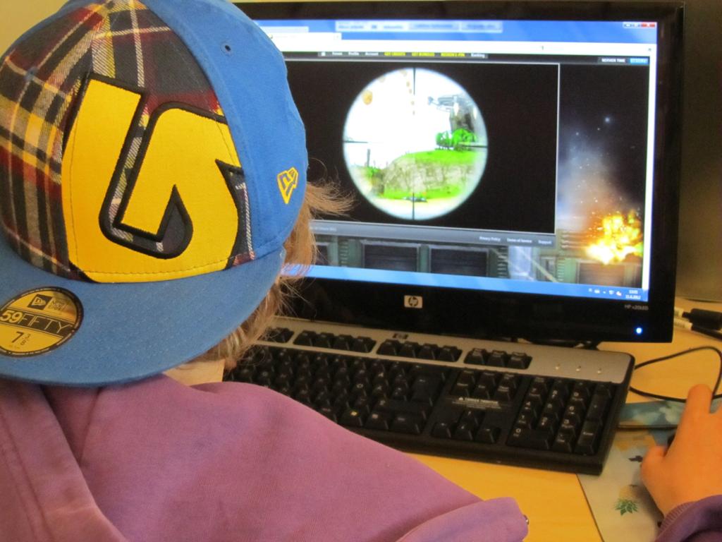 Ung gutt med kaps spiller skytespill på PC. Foto. 