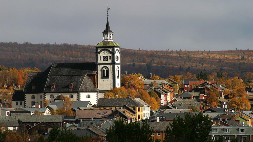 Kirke i ein by. Høstfarger på tre og ås i bakgrunnen. Foto.