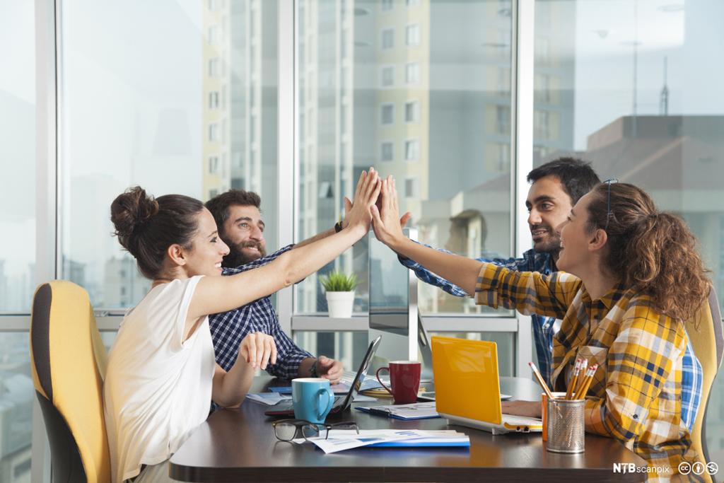 Fire personer gir high five over et konferansebord. Foto.