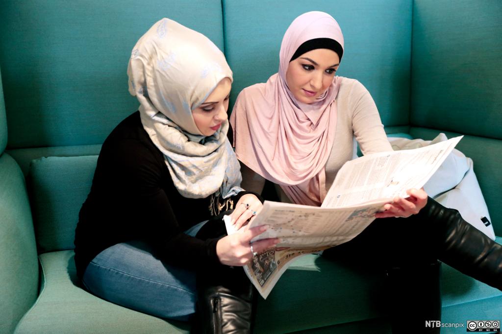 To unge kvinner med hidsjab leser avis. Foto.