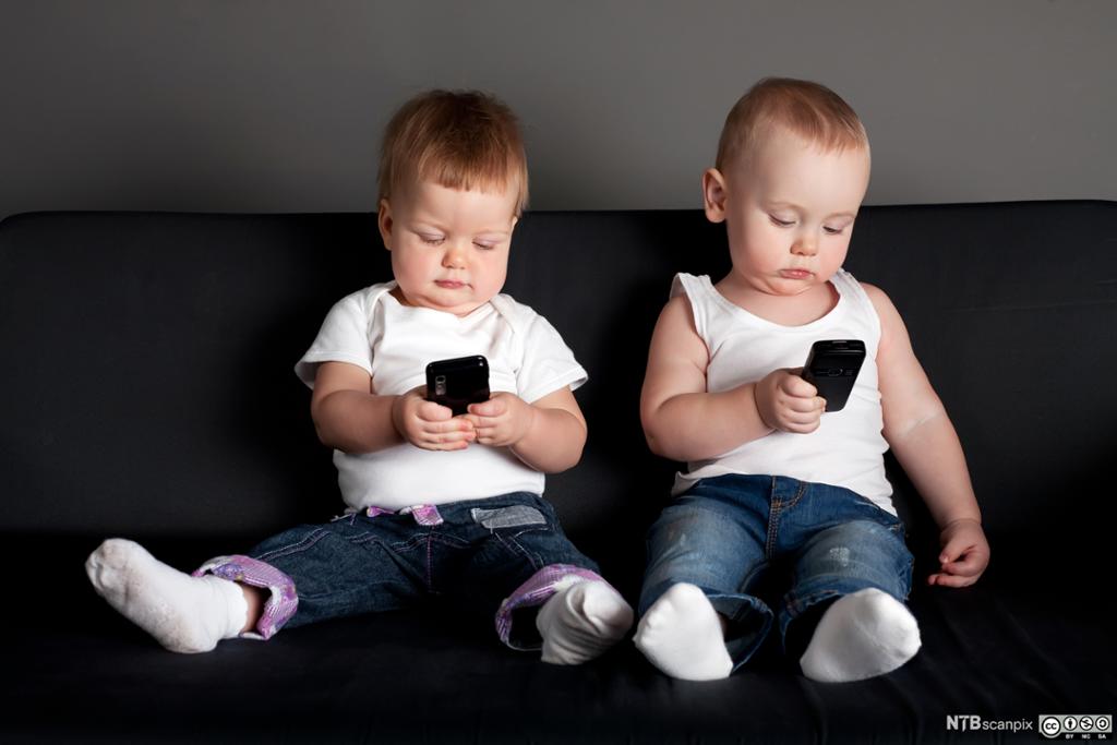 To småbarn ser på hver sin mobil. Foto.