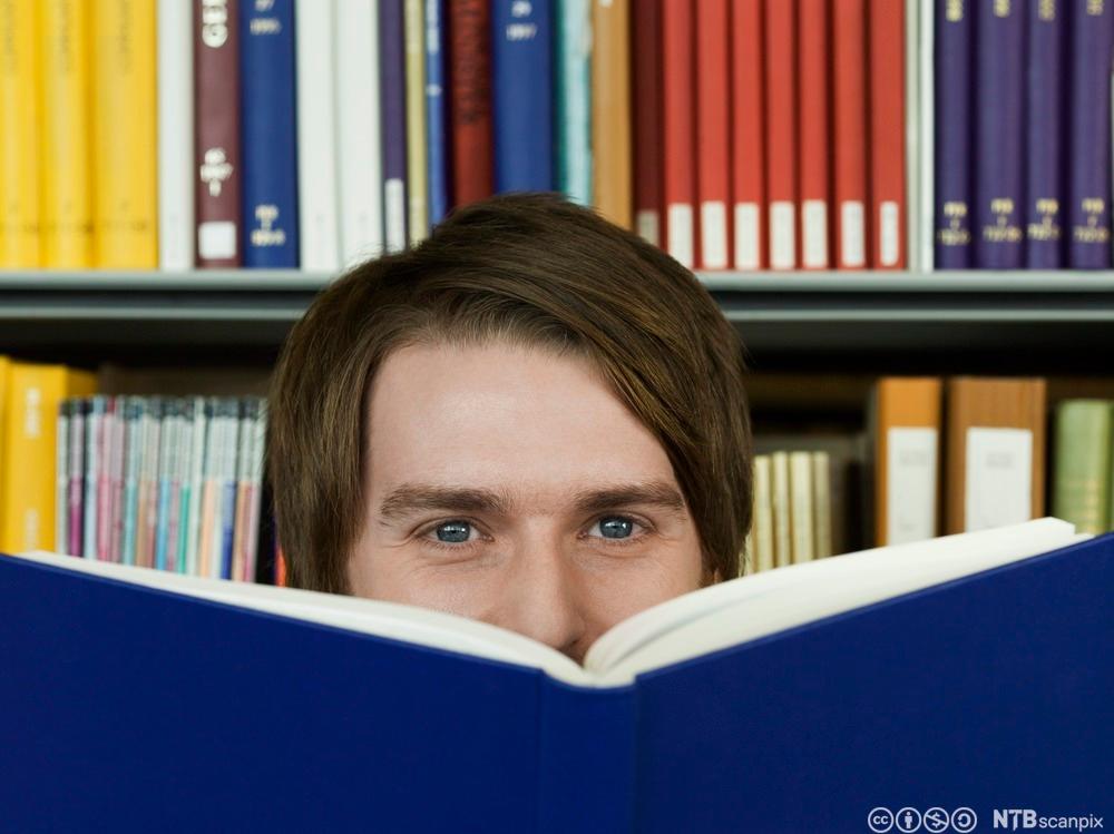 Gutt med ei stor, blå bok foran halve ansiktet. Foto.