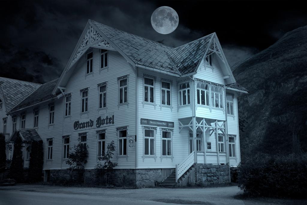 Et gammelt hotell. Hvitmalt trebygning i mørke. Det er natt, men fullmåne. Foto.
