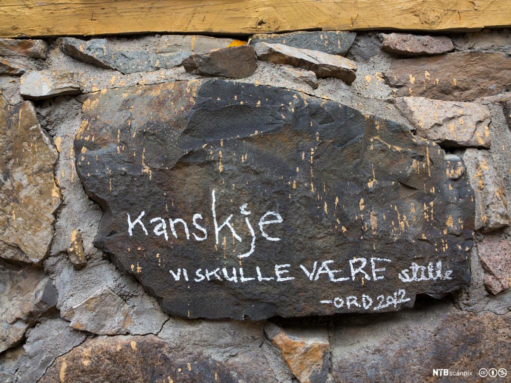 En stein i en gammel gråsteinsmur tagget med teksten Kanskje vi skulle være stille. Foto.