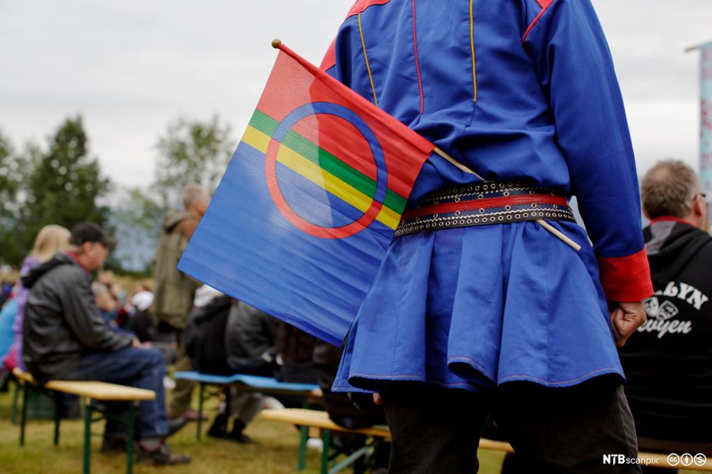En mann i samisk kofte og med samisk flagg. Foto. 