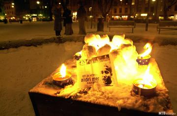 Avisutklipp med bilete av Benjamin Hermansen. Det står framfor ein varde laga av små snøballar med lys i midten. Rundt varden er det fire tende faklar. Foto.