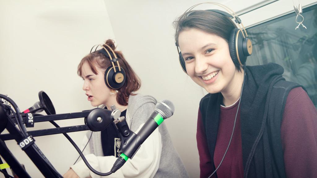 To jenter sitter foran hver sin mikrofon i et lydstudio. Foto.