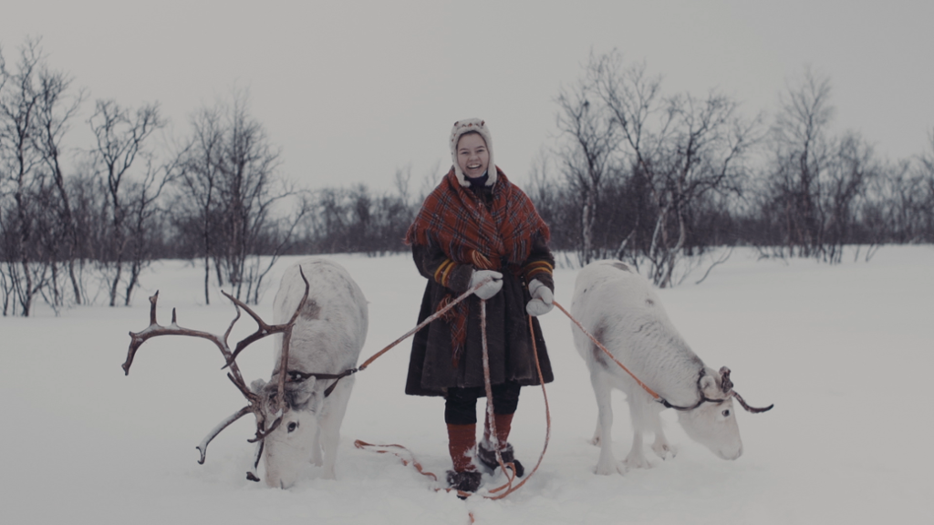 Ung samisk kvinne i tradisjonelle klær, med to reinsdyr. Bilde fra film om identitet og levesett i Sápmi. 