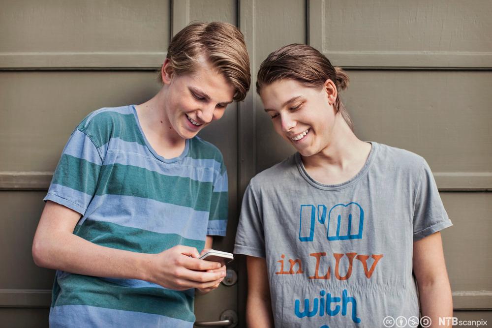 To gutter som ser på en mobilskjerm og ler. Foto. 
