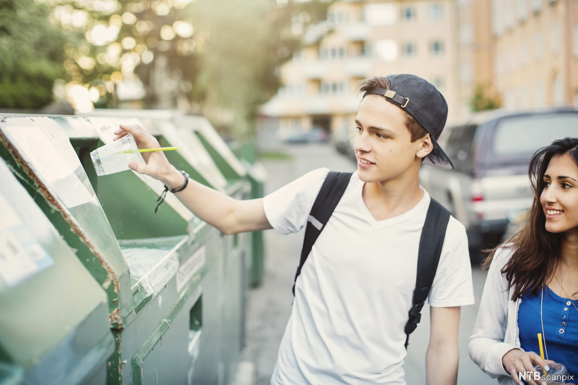 Gutt med kaps kaster plastkopp i søpla. Foto.