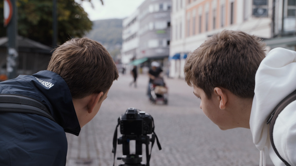 To elever ser mot et kamera som er stilt opp i ei gate. Foto.