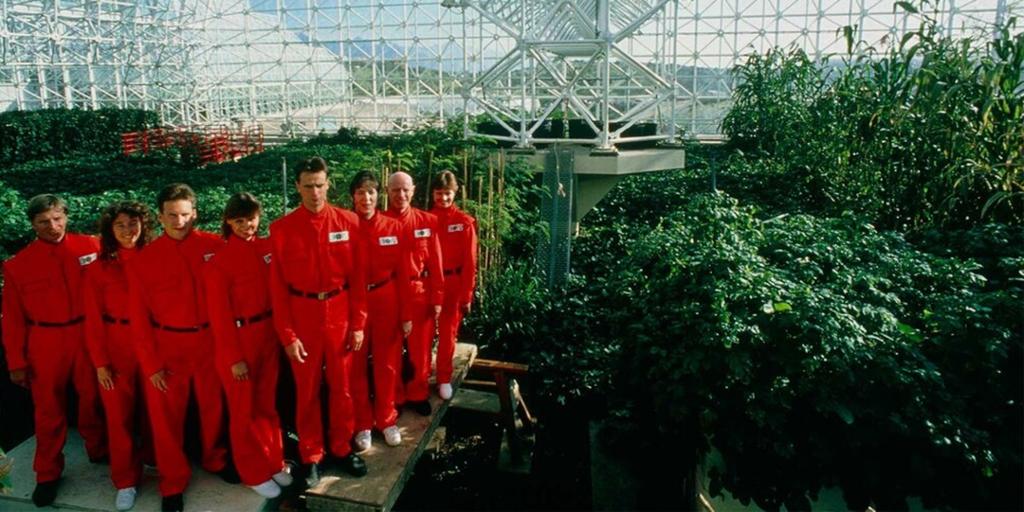 Utsnitt fra filmen Spaceship Earth. Åtte mennesker i røde drakter omgitt av grønne planter.