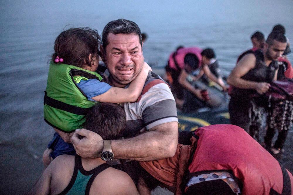 En fortvila far klemmer barna sine etter ei farlig flukt i gummibåt. Foto. 