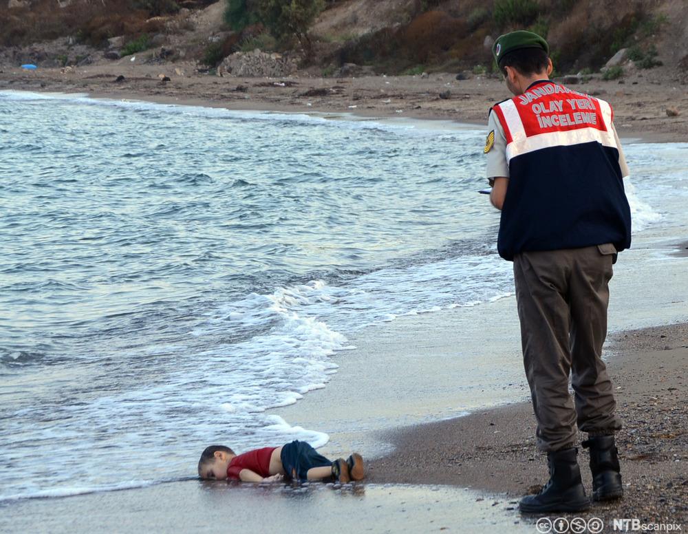 En druknet treåring er skylt på land på en sandstrand. Fotografi.