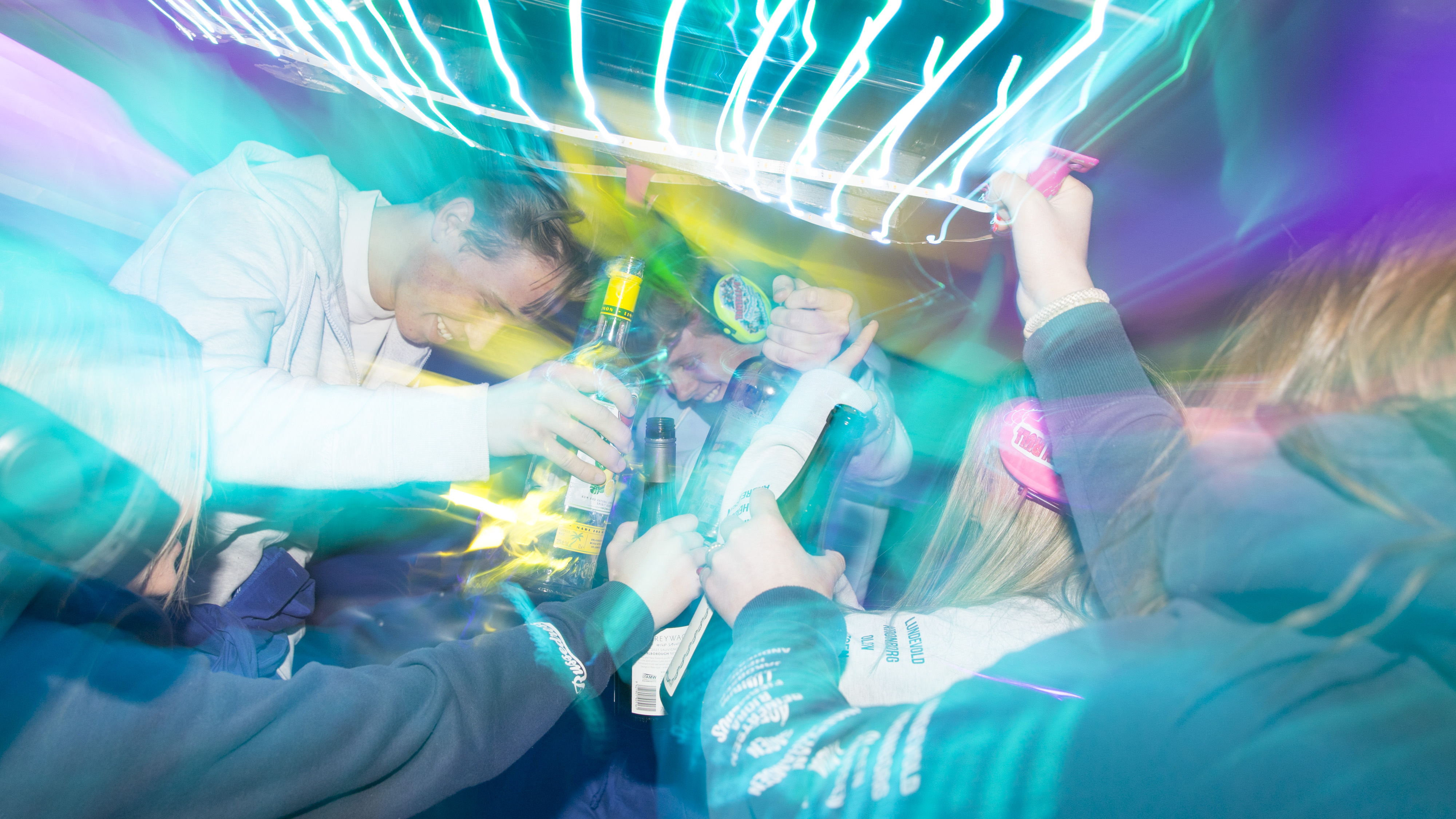 Gutar og jenter i russedressar festar og drikk saman i ein russebuss. Foto.
