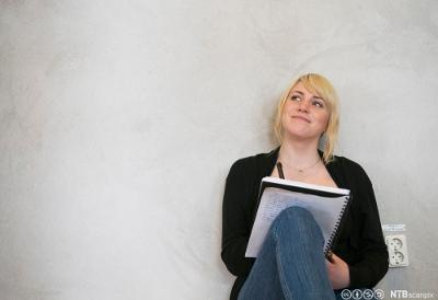 Jente sitter med skriveblokk på knærne og smiler. Foto.