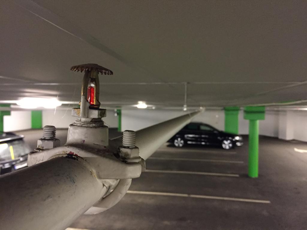 Sprinklerhode og vannrør installert i et parkeringshus. Foto.