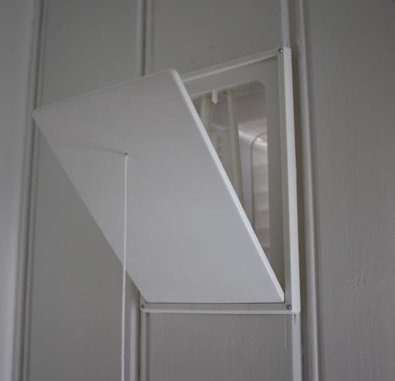 Åpen ventil i en hvit panelvegg innendørs. Foto. 