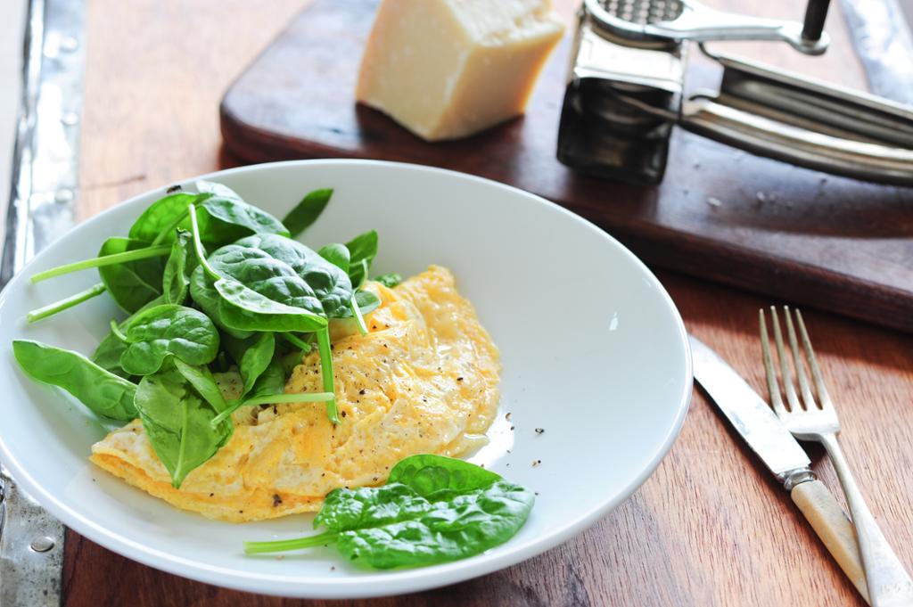 En omelett naturell anrettet på en tallerken med ferske spinatblader ved siden. Foto.