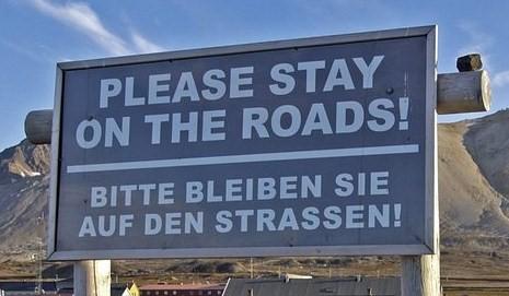 Tospråklig informasjon for turister i Ny-Ålesund: Please stay on the road. Bitte bleiben Sie auf den Straßen.