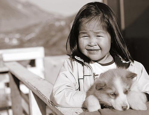 Inuittjente med en hund i hendene. Foto