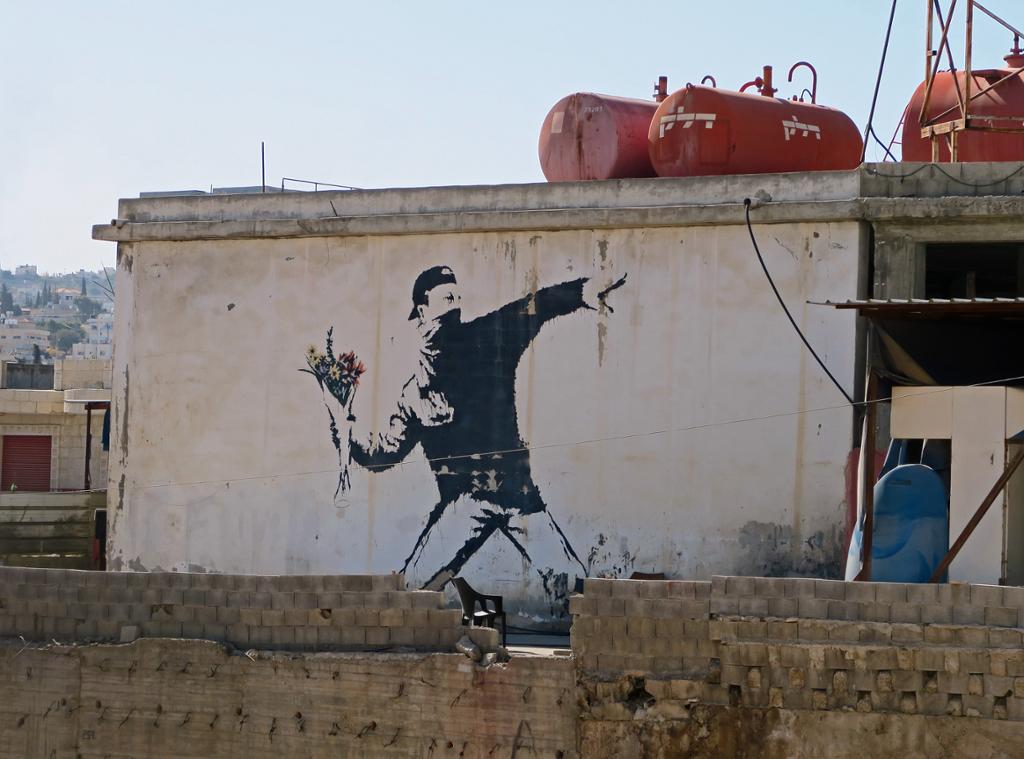 Banksy street art. It depicts a mob that, instead of throwing stones, is throwing a bouquet of flowers. Photo.